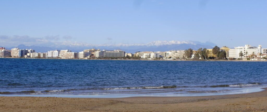 Le front de mer de Roses vu depuis la plage, avec les Pyrénées enneigées à l'horizon